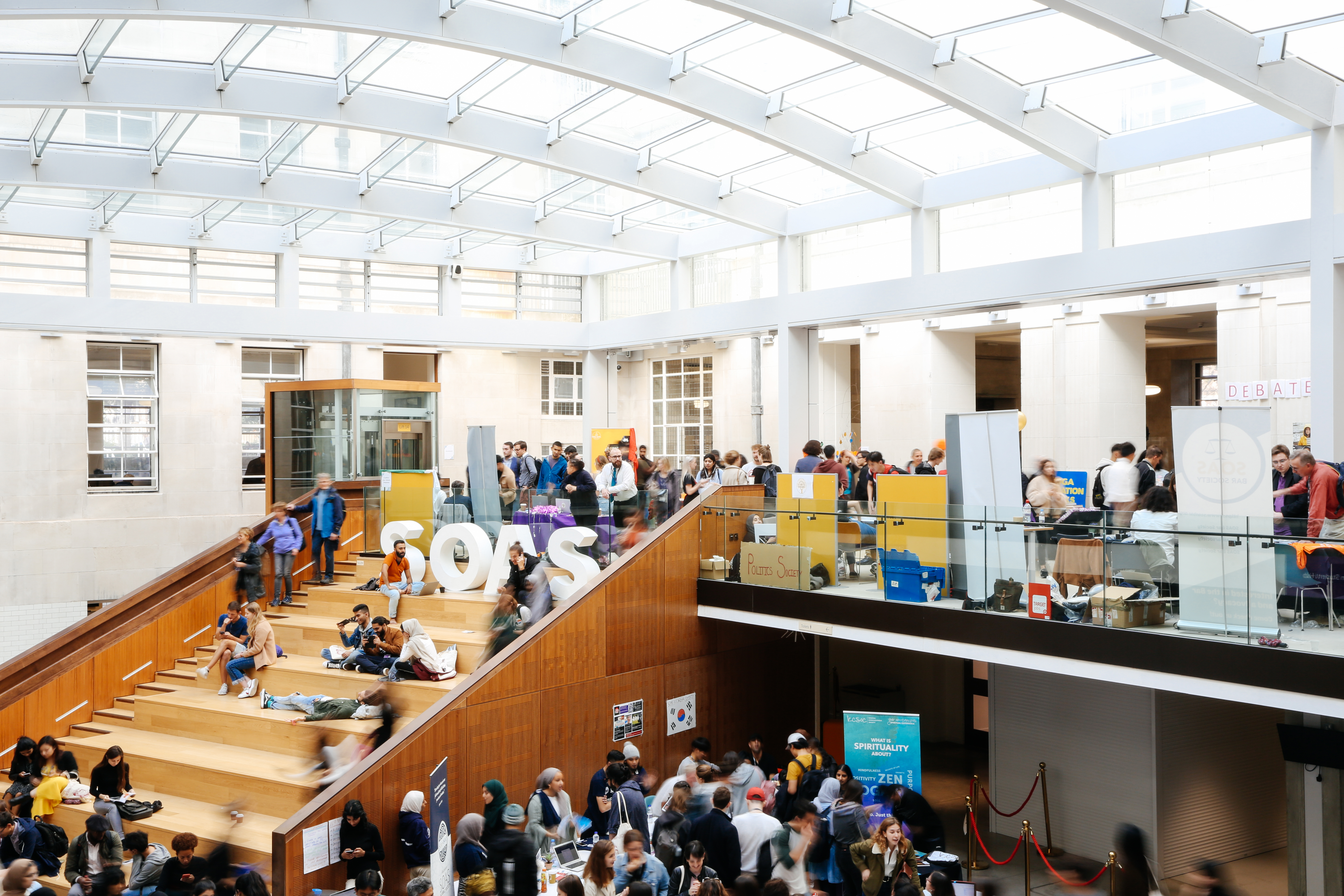 An image of a large internal space within the SOAS building with busy students, staircase, and glass roof.